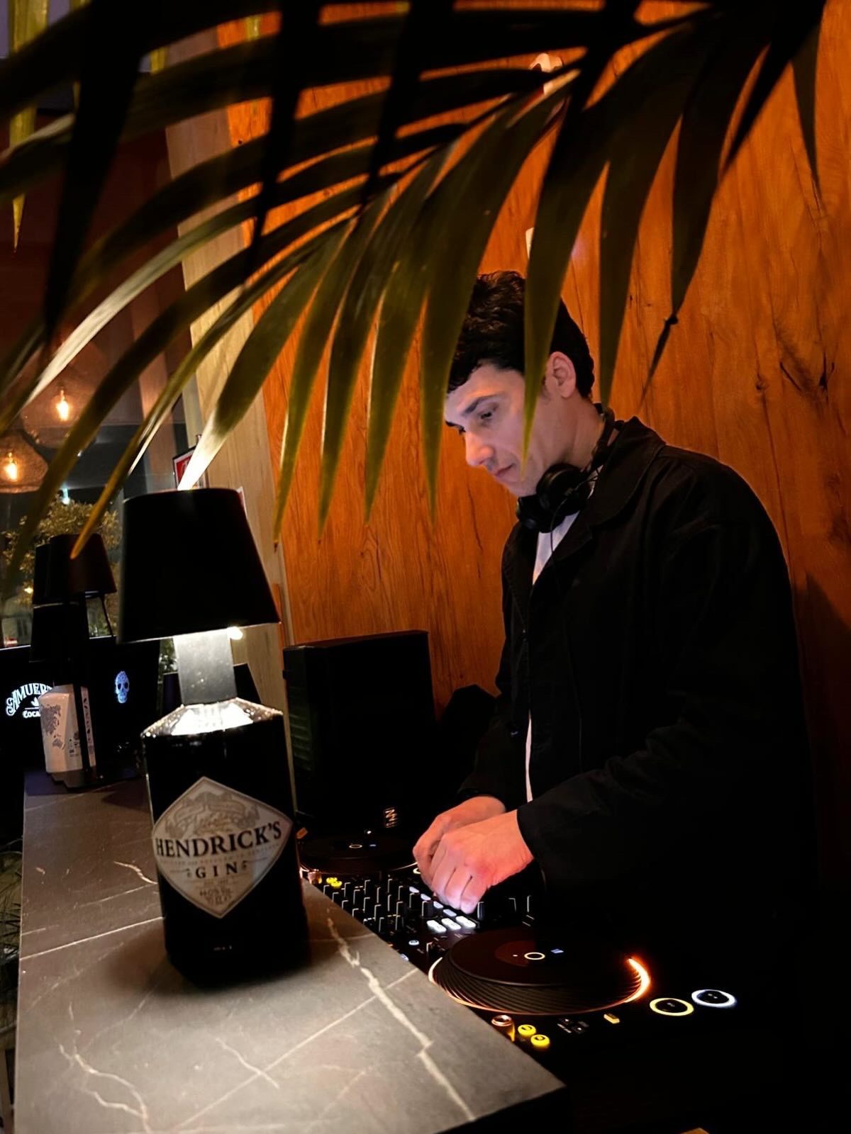 Jam Mattia in papillon alla console di un locale privato a Padova, DJ set elegante tra piante e luci calde