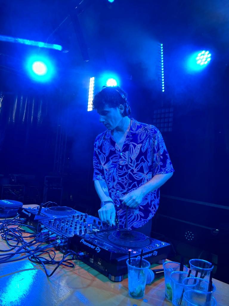 Jam Mattia in DJ set house ed elettronico a un evento pubblico, su palco con luci blu e fumo