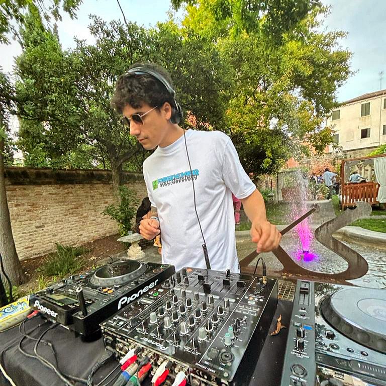 DJ set al Lido di Venezia: Jam Mattia alla console Pioneer in giardino con cuffie e occhiali da sole, evento estivo a Venezia
