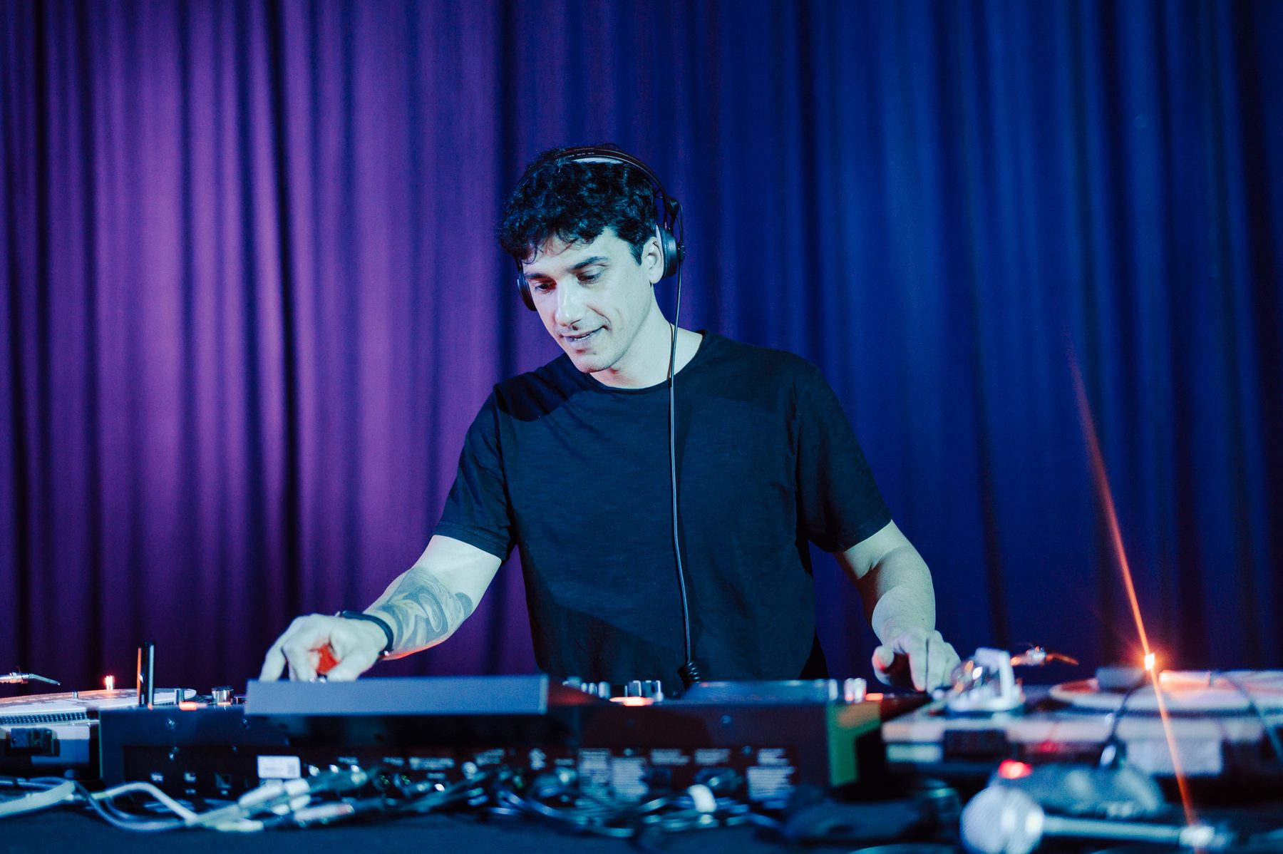 Jam Mattia in DJ set per una festa corporate davanti a un tendaggio viola, console e giradischi