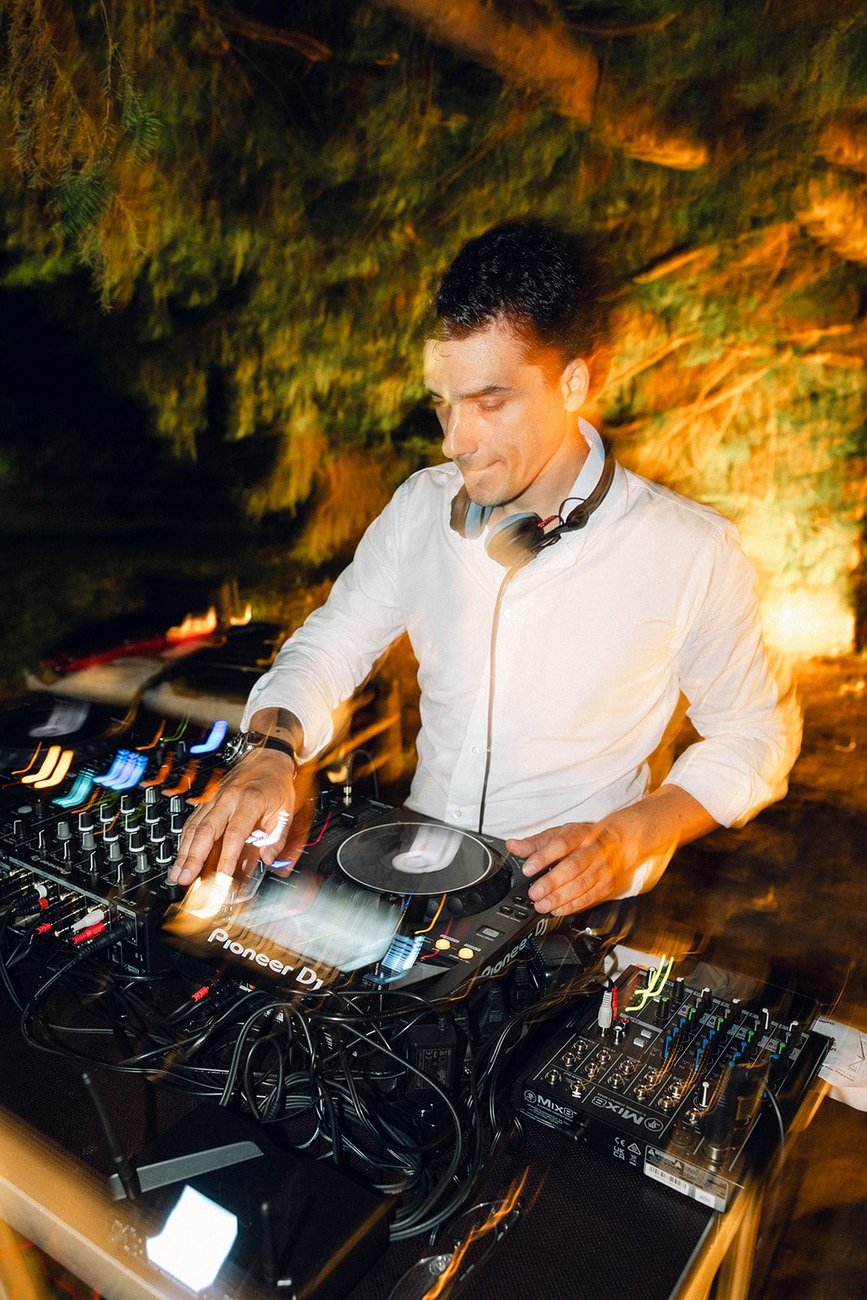 Jam Mattia in camicia bianca alla console con cuffie, DJ set serale di matrimonio a Villa Ca' Sagredo tra le luci calde del giardino