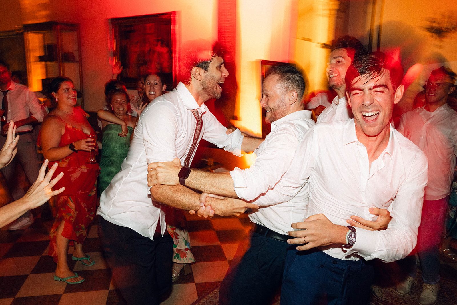 Invitati che ridono e ballano abbracciati a Villa Ca' Marcello (Padova) durante il DJ set di matrimonio, luci arancioni e pavimento a scacchi