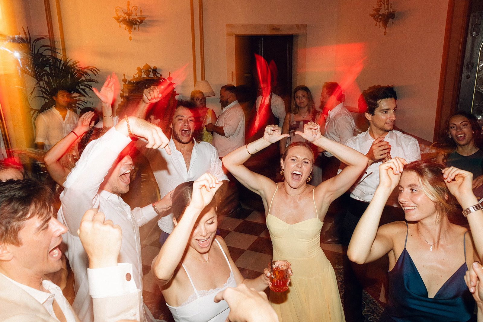 Festa di matrimonio a Villa Sagredo (Vigonovo, Venezia): invitati che ballano a braccia alzate nel salone illuminato di rosso durante il DJ set