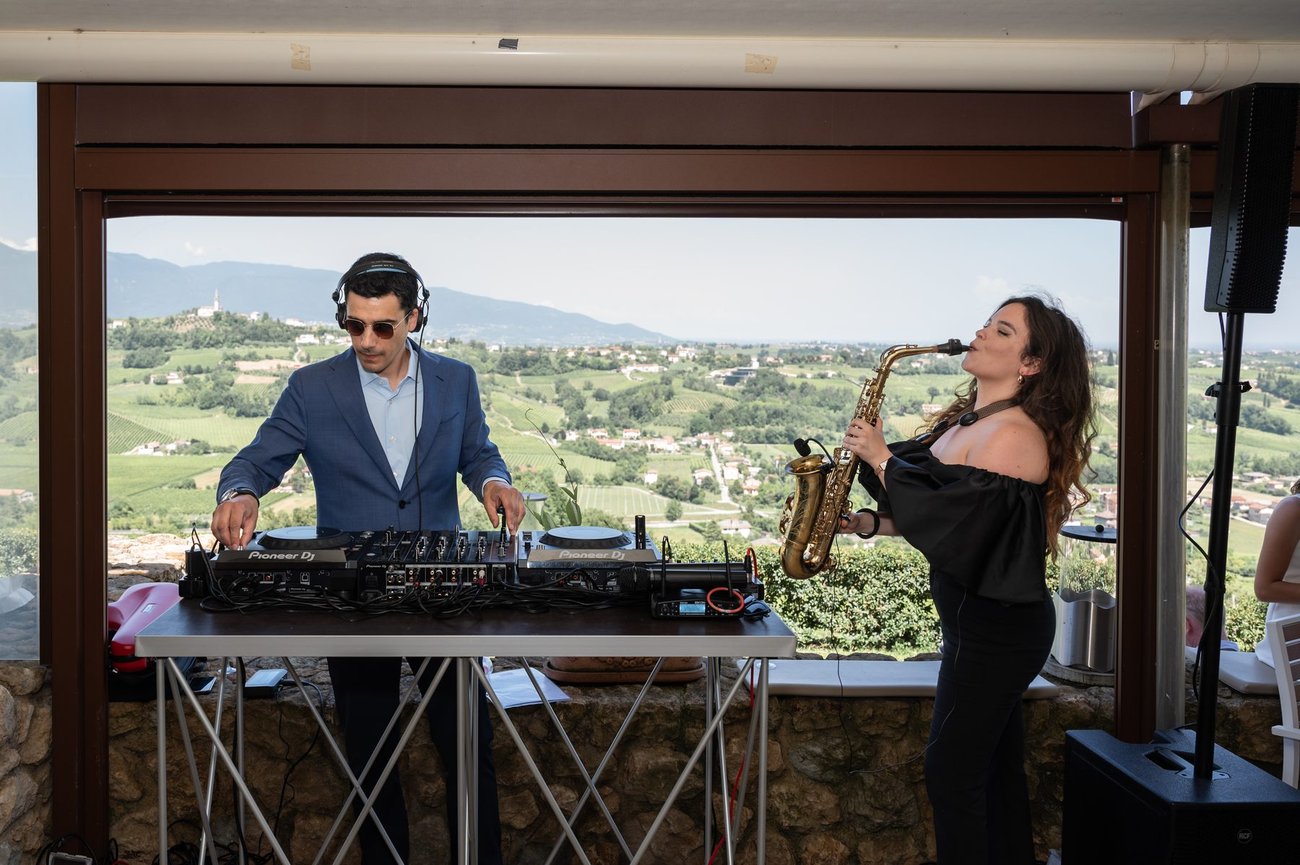 DJ set più sax live su una terrazza con vista sulle colline: Jam Mattia alla console e la sassofonista accanto, aperitivo di matrimonio