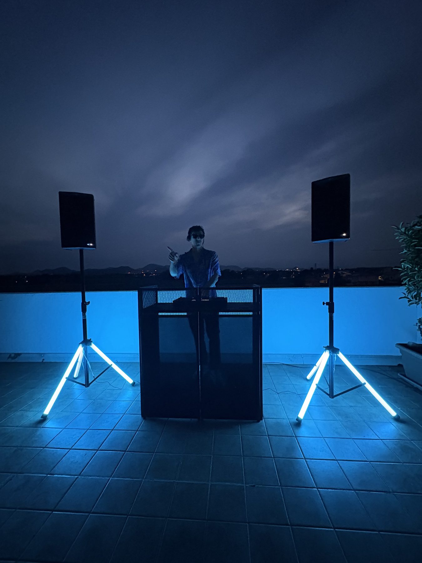Setup esterno completamente a batteria all'ora blu: due casse su stativo con luci led e postazione DJ in controluce, nessun collegamento alla corrente